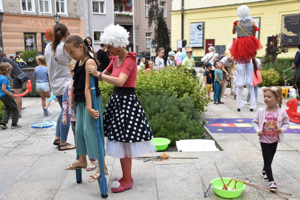Dziewczynka uczych chodzić się na szczudłach, pomaga jej klaun