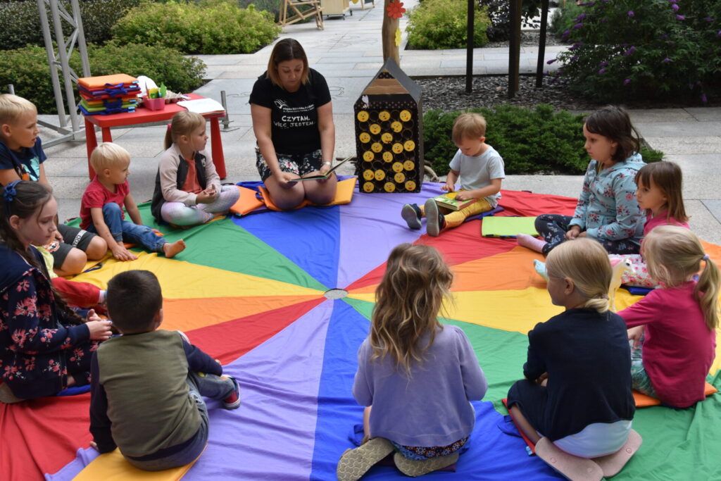 Dzieci słuchają czytanej bajki, siedzą na kolorowej chuście
