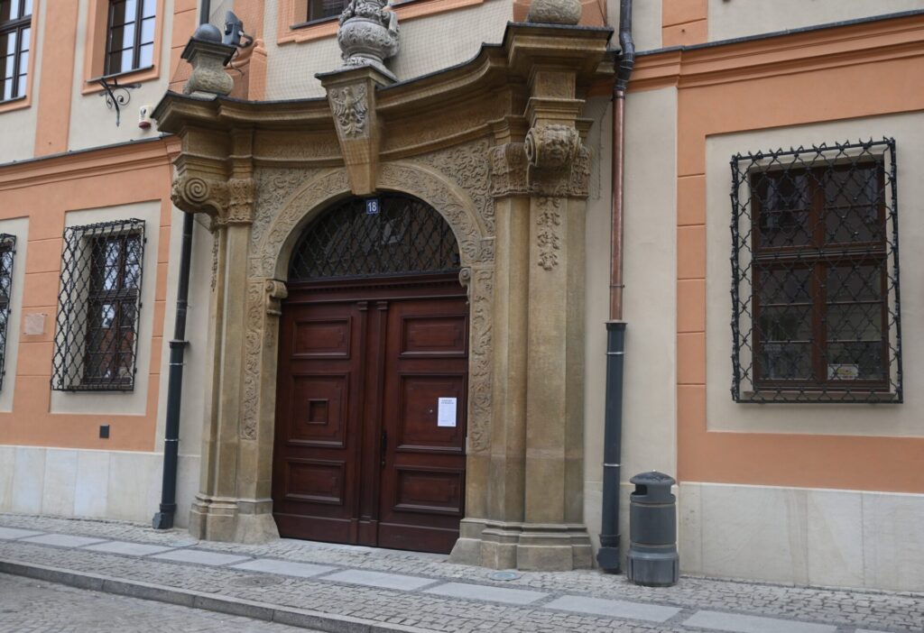 Bogato zdobione wejście do zabytkowego budynku z masywnymi drewnianymi drzwiami, kamiennym portalem.