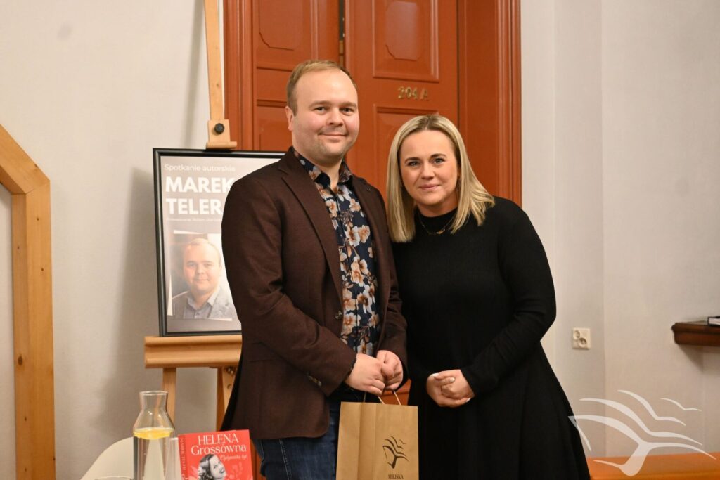 Marta Wojciechowska i Marek Teler stoją. Marek Teler trzyma w rękach torbę z logo biblioteki.