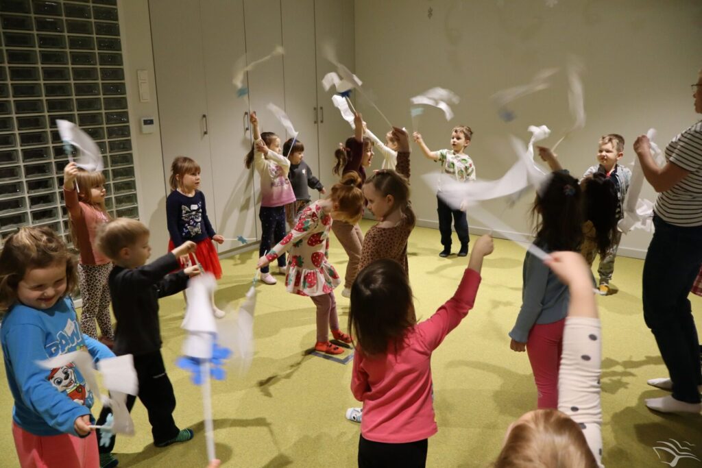 Dzieci chodzą w kółko i machają białymi chorągiewkami z papieru.