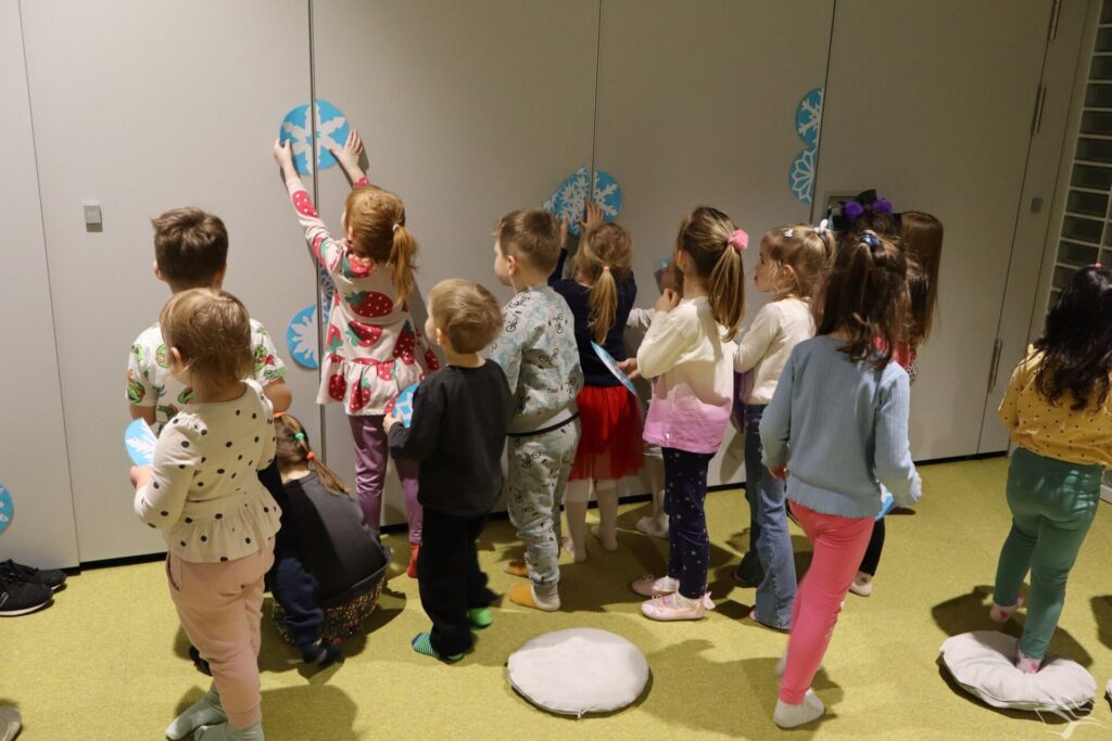 Dzieci przyklejają połówki śnieżynek zrobionych z papieru do szafy.