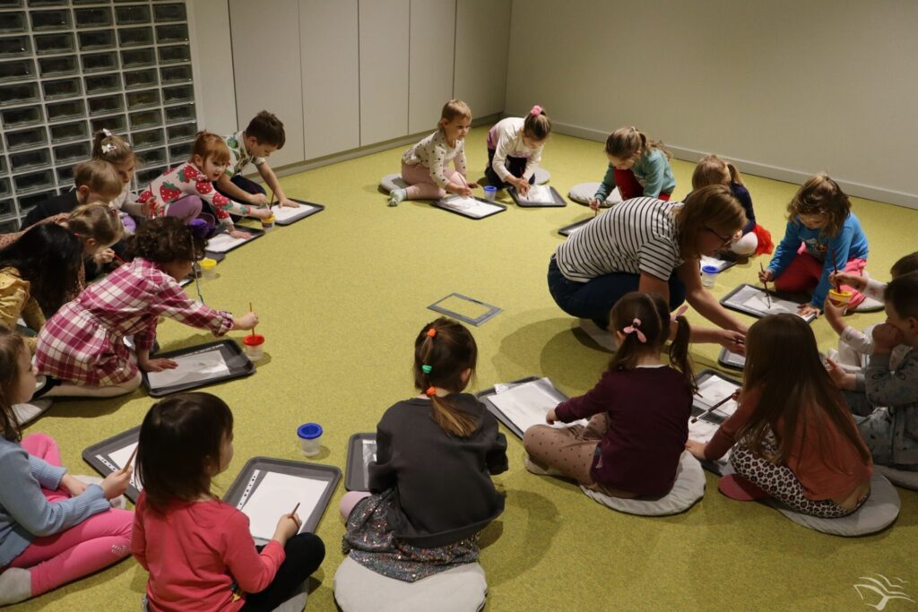 Dzieci siedzą na dywanie i malują.