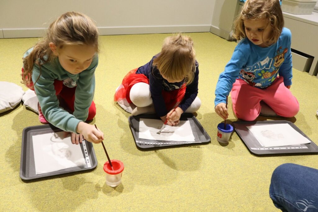 Dzieci siedzą na dywanie i malują.