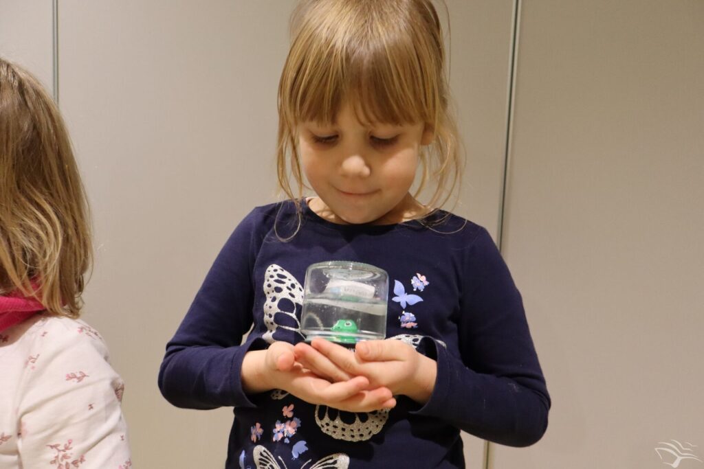 Dziewczynka trzyma w rękach szklaną kulę zrobioną ze słoika. 