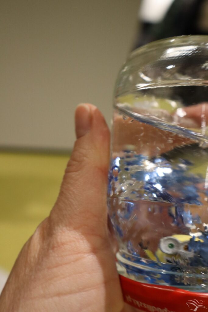 Słoik z wodą, brokatem i figurką w środku.